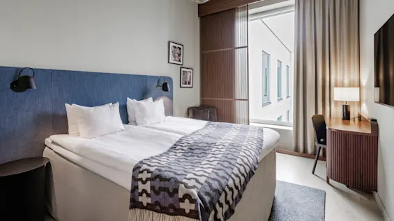 A neatly arranged hotel room with a double bed, ambient lighting, and modern decor, showcasing comfort and simplicity.