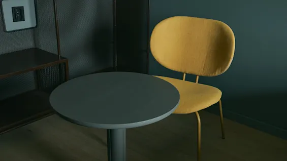Ett stilrent hotellrum på Stopover Hotel Falkenberg med ett mörkt runt bord och en ljusgul stol.