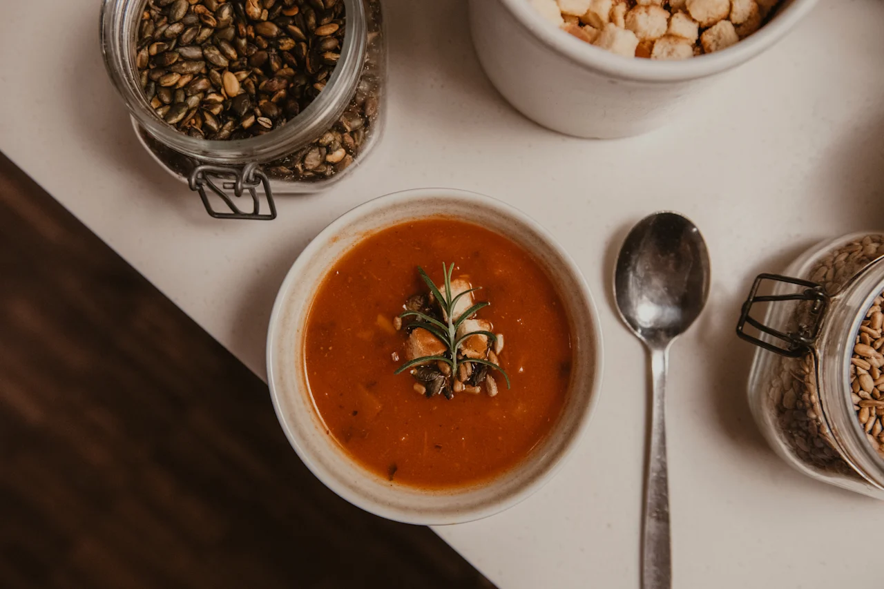 En varm skål suppe, garneret med friske urter og frø, klar til at blive nydt med en ske og diverse toppings.