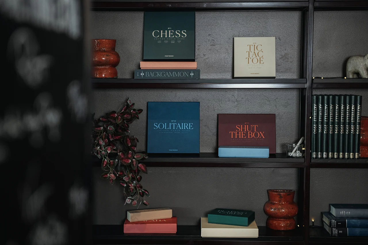 En mysig bokhylla fylld med klassiska brädspel som Chess, Tic Tac Toe, Solitaire, Backgammon och Shut The Box, tillsammans med böcker.