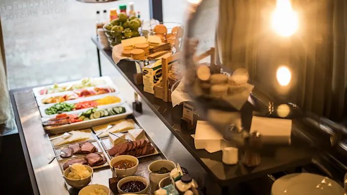 En frokostbuffé med forskjellige matvarer utstilt på en benk, varmt opplyst inne i en restaurant.