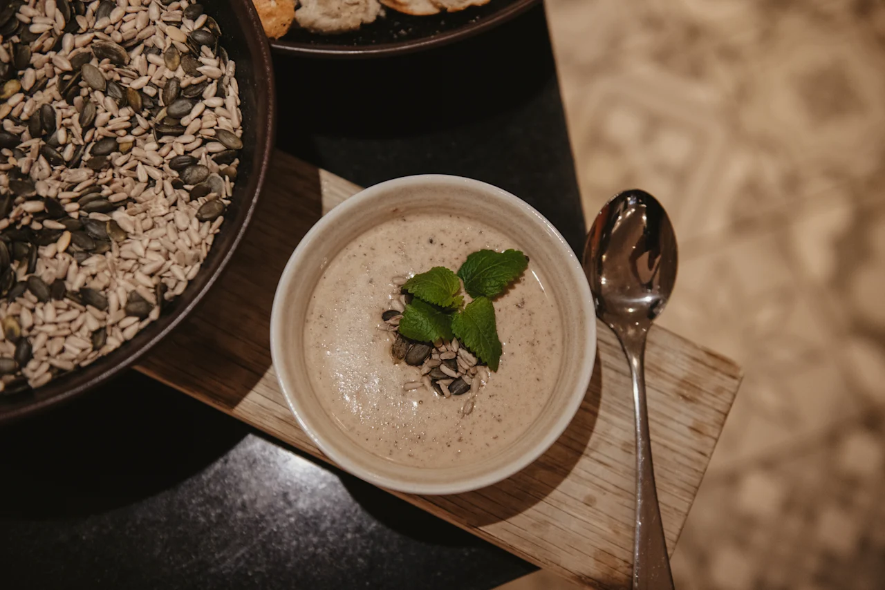 En närbild av en krämig rätt garnerad med mynta och frön, serverad med en sked och en skål med frön. Home Hotel Grand, Helsingborg.