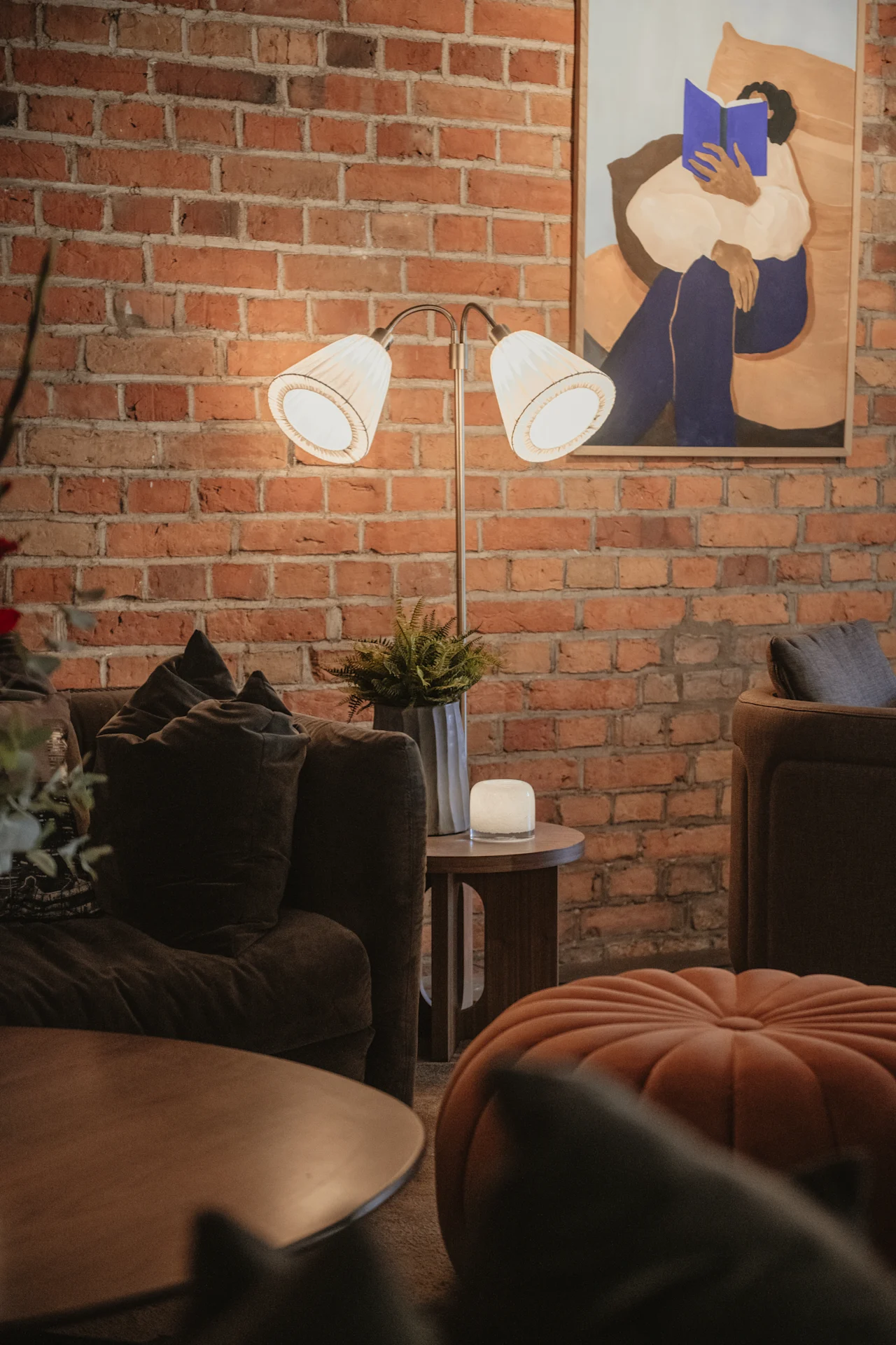 Et varmt, indbydende rum med en murstensvæg, blød belysning og en komfortabel sofa. Et maleri viser en person fordybet i en bog.