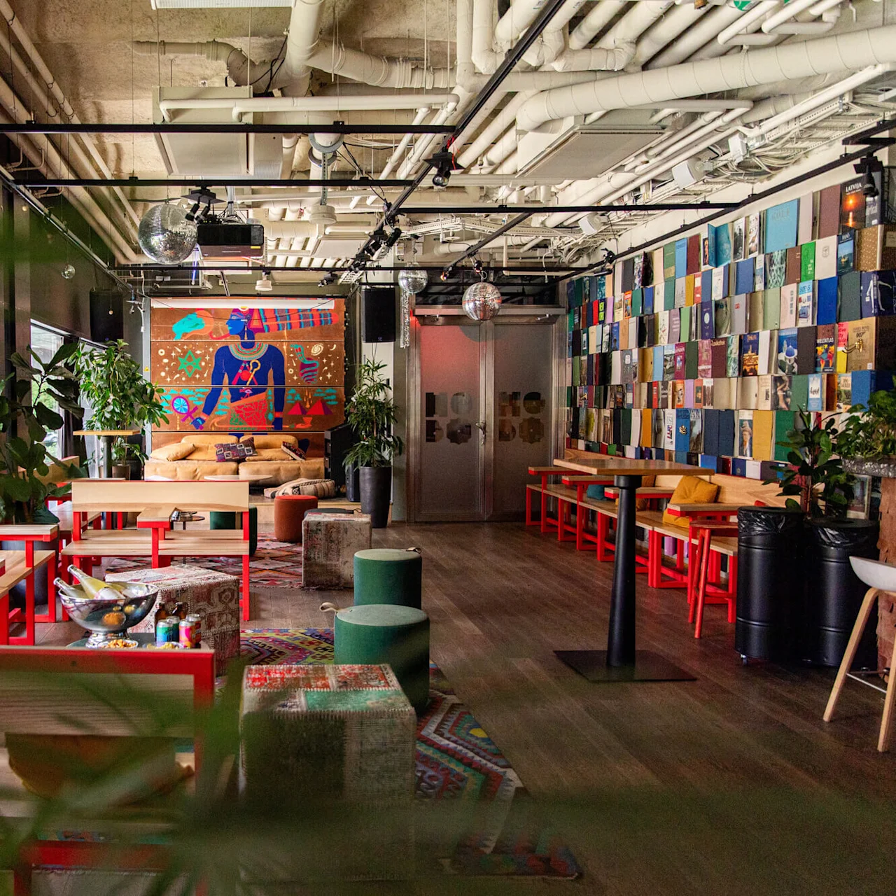 A modern lounge with colorful furniture and artwork on the walls; lush indoor plants add greenery, with tables and seating arranged for socializing and relaxation.