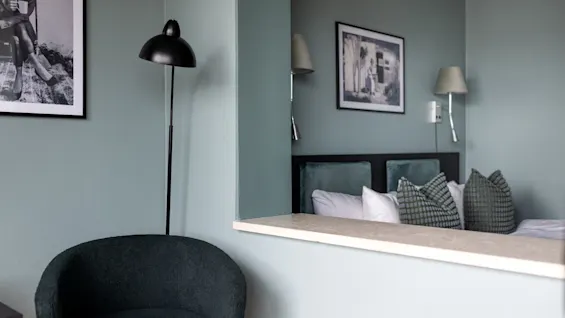 Et moderne hotellrom med en komfortabel seng og et separat salongområde, med stilig innredning og myk belysning.