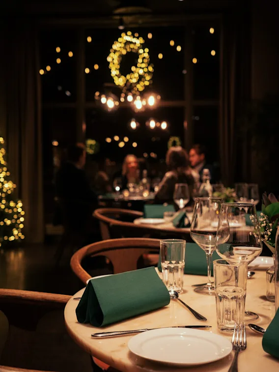 Koselig restaurant dekket til middag med varm julebelysning og gjester i bakgrunnen