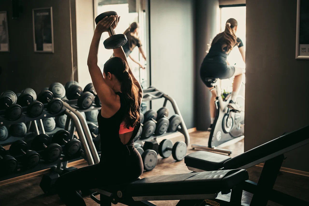Folk træner i et fitnesscenter, en løfter vægte og en anden på en motionscykel.