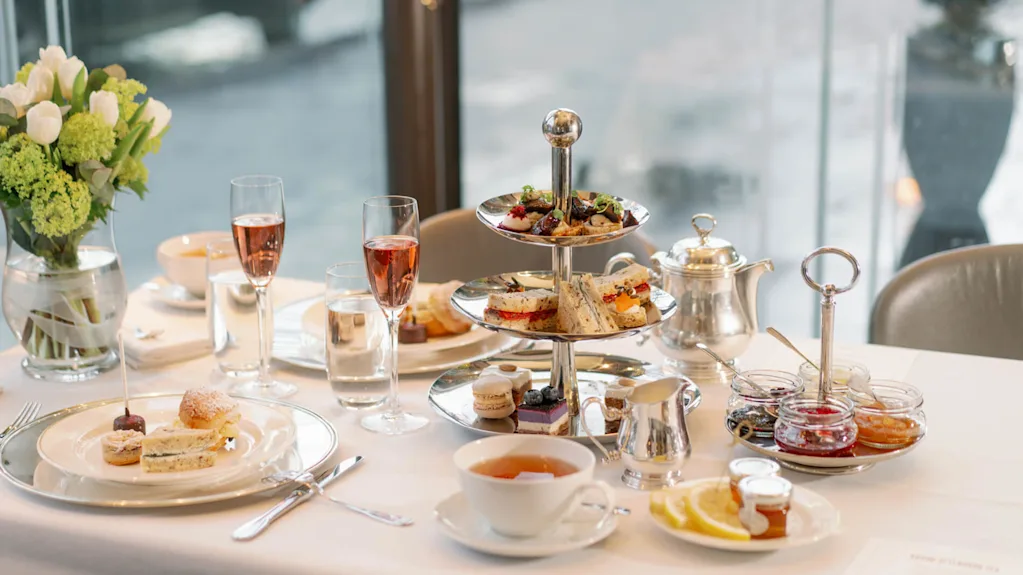 En elegant afternoon tea-dukning med ett treskikts kakfat fyllt med smörgåsar och bakverk, samt tillhörande drycker på ett bord på Hotel Kämp i Helsingfors.