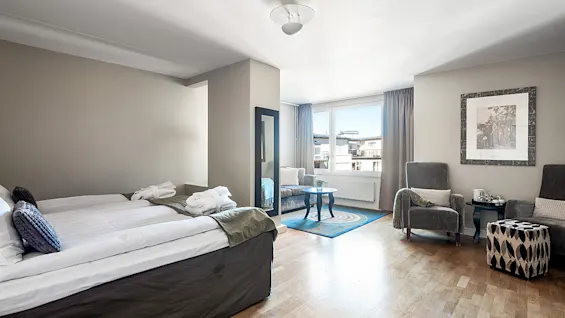 A neat bedroom-living room space with a bed, chairs, and a table by a balcony in a well-lit apartment.