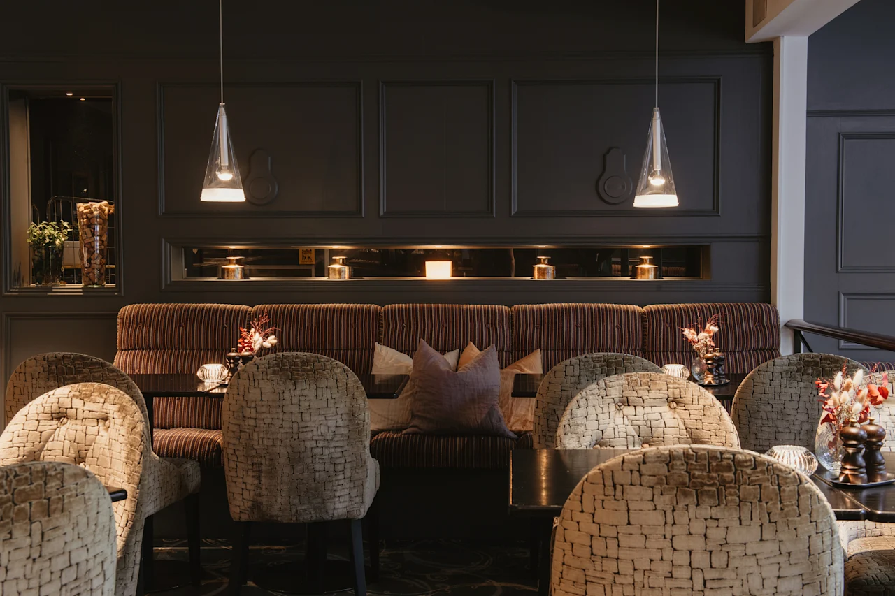 A cozy dining area at Home Hotel Kung Oscar with banquette seating, textured chairs, and warm lighting, perfect for a relaxing meal.