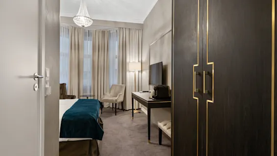 Et velindrettet hotelværelse med en komfortabel seng, en funklende lysekrone, et skrivebord med TV og et elegant klædeskab.