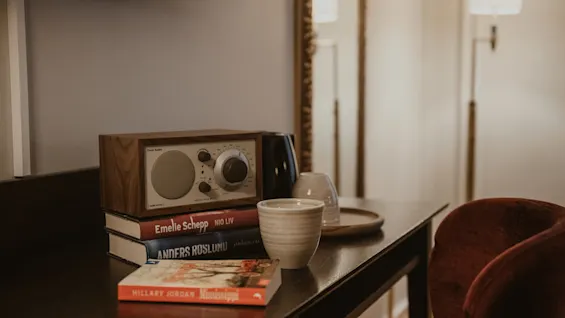 A cozy reading nook with a radio, books (NIO LIV, Anders Roslund, Mississippi), and a cup. Home Hotel Kung Oscar.