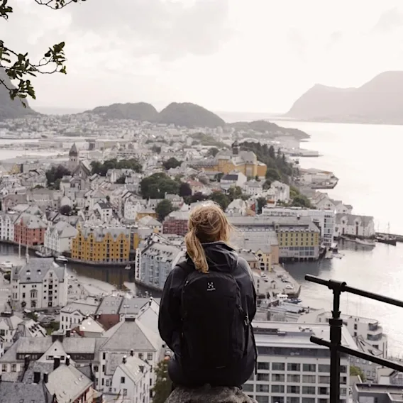 En kvinne med sekk sitter på Fjellstua utkikkspunkt med utsikt over Ålesund by.