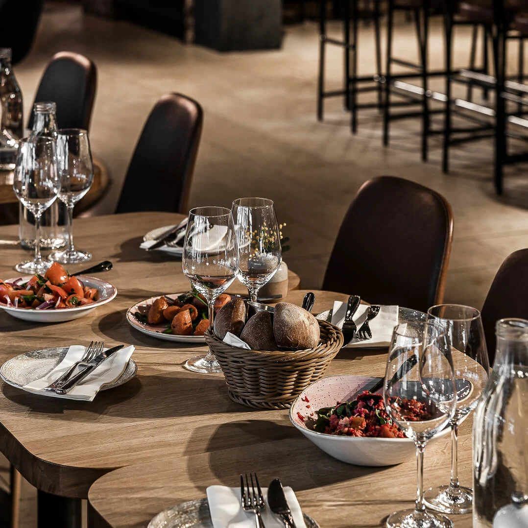 Ett väldukat matbord med tallrikar, bestick och glas, antyder en kommande måltid, mot en bakgrund av en exklusiv restaurang.