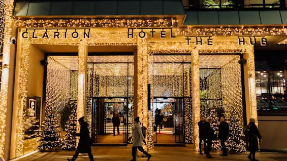 Människor som går förbi en hotellentré vackert dekorerad med glödande gyllene julbelysning.