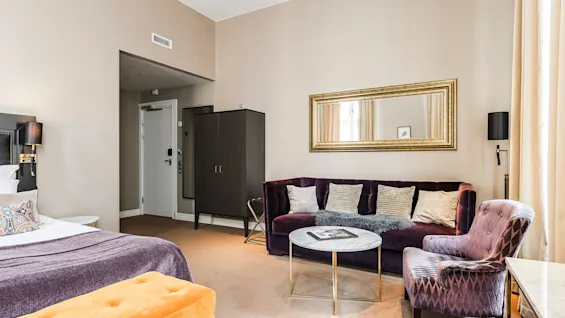 Ett välarrangerat hotellrum med säng, soffa, stolar och spegel som utstrålar komfort och elegans.