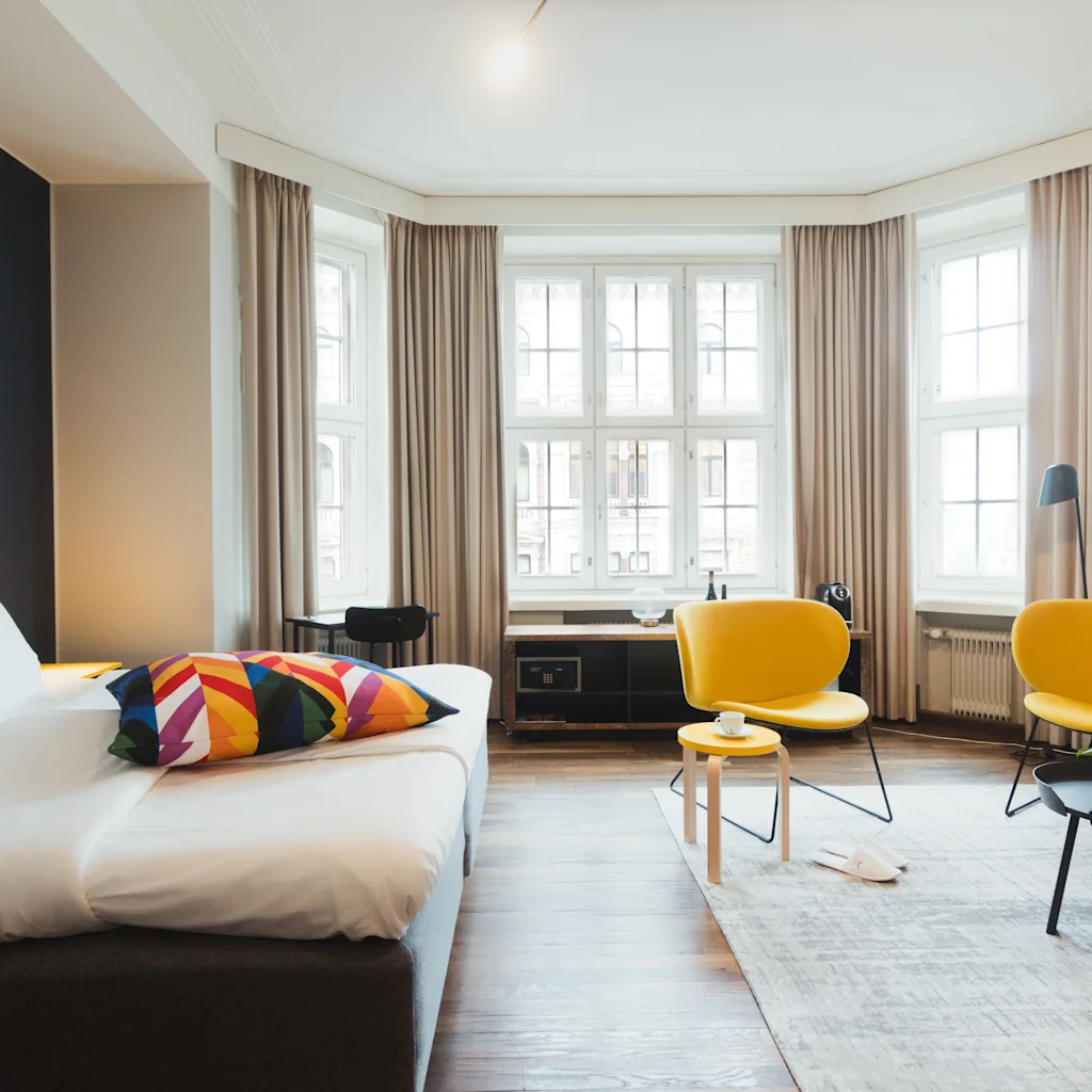 Valoisa hotellihuone, jossa on mukava sänky, kaksi keltaista tuolia ja suuret ikkunat, luo kutsuvan ja rentouttavan tunnelman.