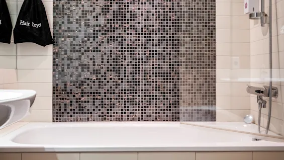 Moderni kylpyhuone, jossa on kylpyamme ja suihku, mosaiikkilaatoitettu seinä ja pussi, jossa lukee Hair Dryer.