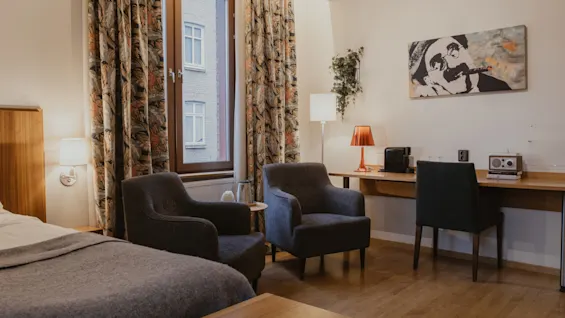 A well-appointed hotel room with a bed, comfortable seating, and a functional workspace. Home Hotel Kung Oscar.