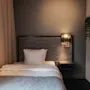 A cozy hotel room with a single bed, bedside lamp, and a plant, creating a comfortable and inviting atmosphere.