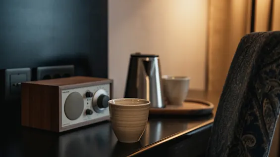 En mysig hörna med en radio, vattenkokare och koppar på ett mörkt bord, vilket antyder en avkopplande stund med musik och en varm dryck.