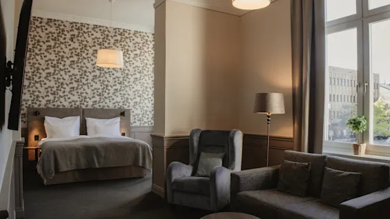 Ett välutrustat hotellrum med både ett vilsamt sovrum och en bekväm sittgrupp med naturligt ljus.