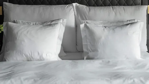 A neatly made hotel bed with white pillows in a hotel room with a black tufted headboard and modern wall lamps.