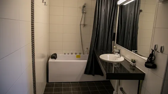 Modern bathroom featuring a bathtub, dark shower curtain, and a stylish sink with a large mirror.