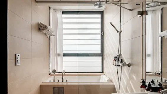 A bright and modern bathroom at Farris Bad with a bathtub, shower, and a large window with blinds and curtains.
