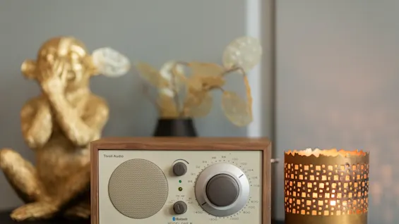 En radio i vintagestil står på en hylle ved siden av en gyllen apestatue og en glødende lysholder.