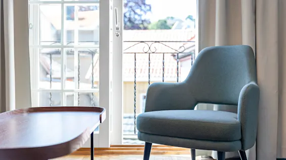 A modern chair and table near an open door leading to a balcony with urban views.