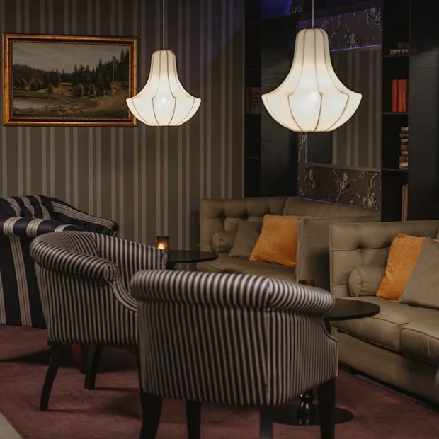 Viihtyisä hotellin oleskelutila, jossa on raidallisia nojatuoleja, mukava sohva ja tyylikkäitä riippuvalaisimia, täydellinen rentoutumiseen.