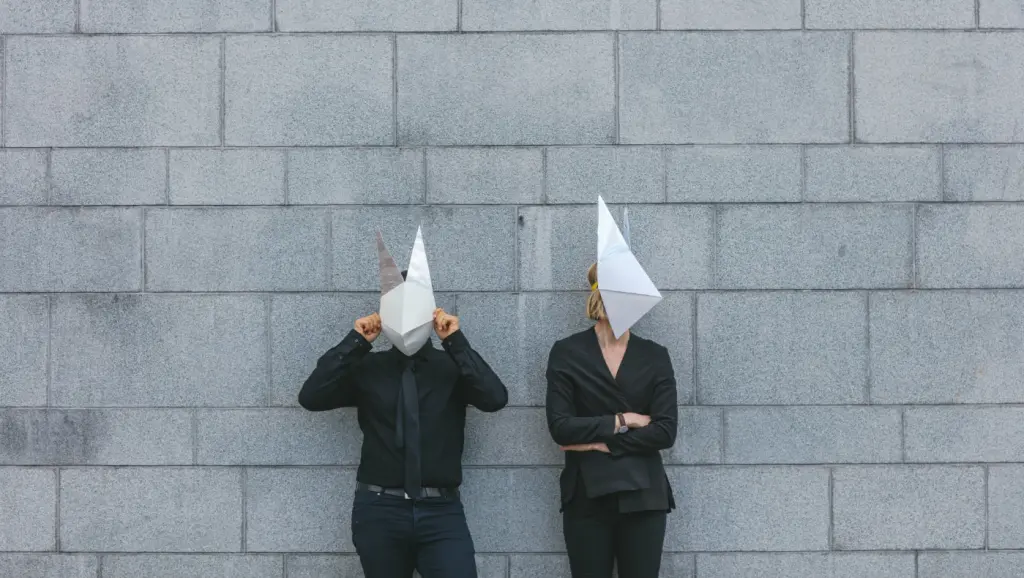 Couple with paper masks against a concrete wall
