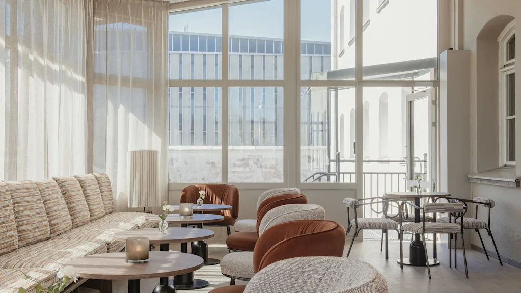 A bright and inviting lounge area with comfortable seating, small tables, and large windows looking out onto an urban scene.