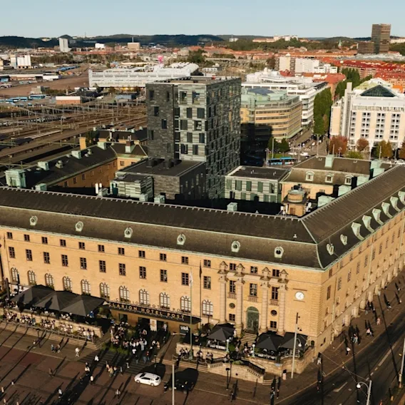 En flygbild av Clarion Hotel Post, en ståtlig byggnad i en livlig stad, med människor och bilar på gatorna och en kanal i närheten.
