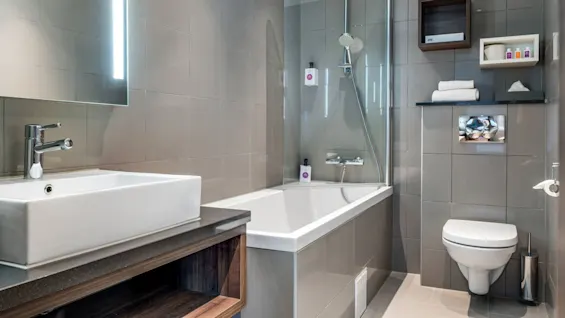 A modern bathroom with a rectangular basin, glass shower partition, and wall-mounted toilet, in a grey tiled setting.