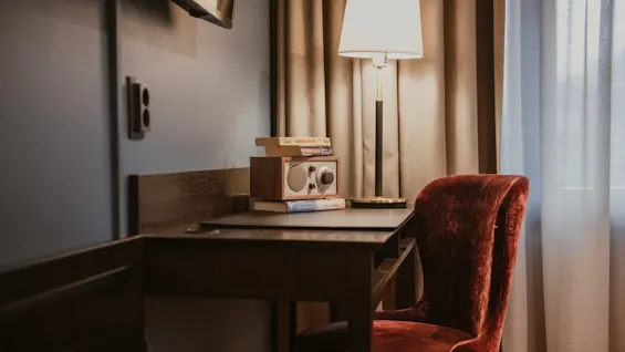 A warm and inviting desk space with a glowing lamp, books, and a vintage radio. Home Hotel Kung Oscar.