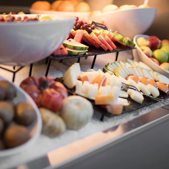 Assorterte oppskårne frukter og hele frukter i boller og brett vises på en buffetbord i et godt opplyst spiseområde.