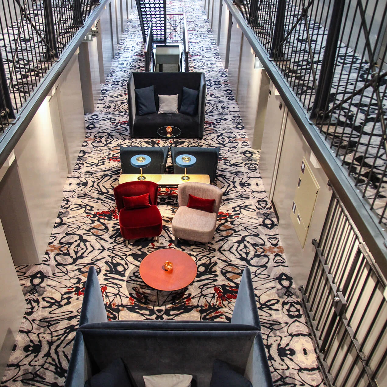 An elevated walkway with chairs and tables, symmetrically arranged, featuring a patterned carpet; contemporary interior design.