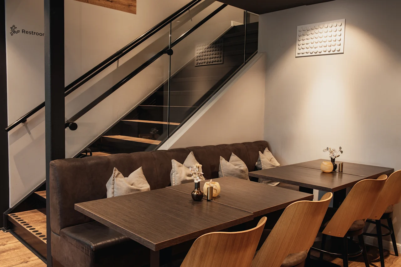 Et moderne og indbydende interiør med komfortable båse, træborde og en elegant trappe. Et skilt indikerer Restroor.