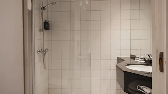 Ett rent, modernt badrum med ett kaklat duschutrymme och en elegant svart kommod med ett vitt handfat.