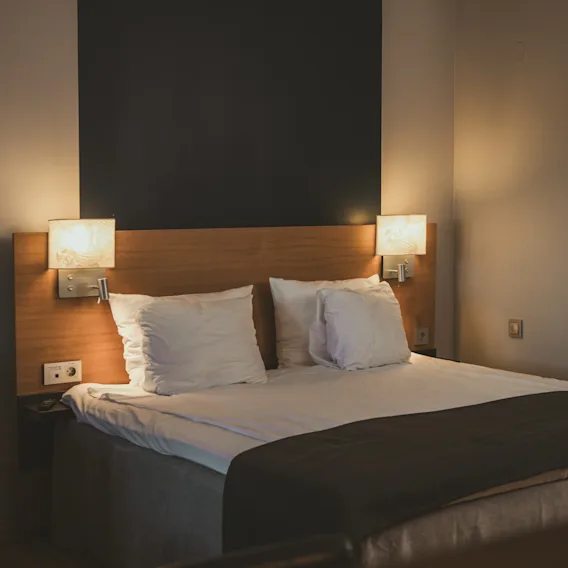Ett mysigt hotellrum med en prydligt bäddad säng, upplyst av varma sänglampor, inbjudande till avkoppling.