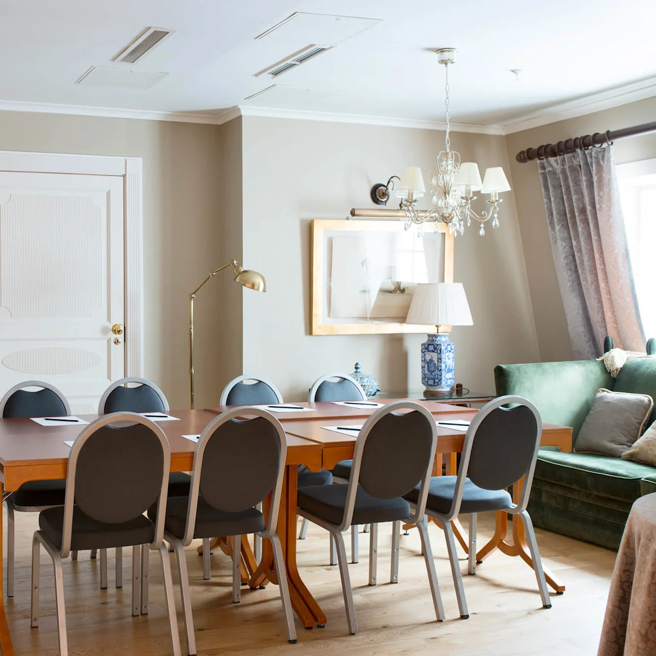 Et elegant møblert rom med et langt spisebord omgitt av stoler, under en lysekrone, som indikerer en luksuriøs innredning.