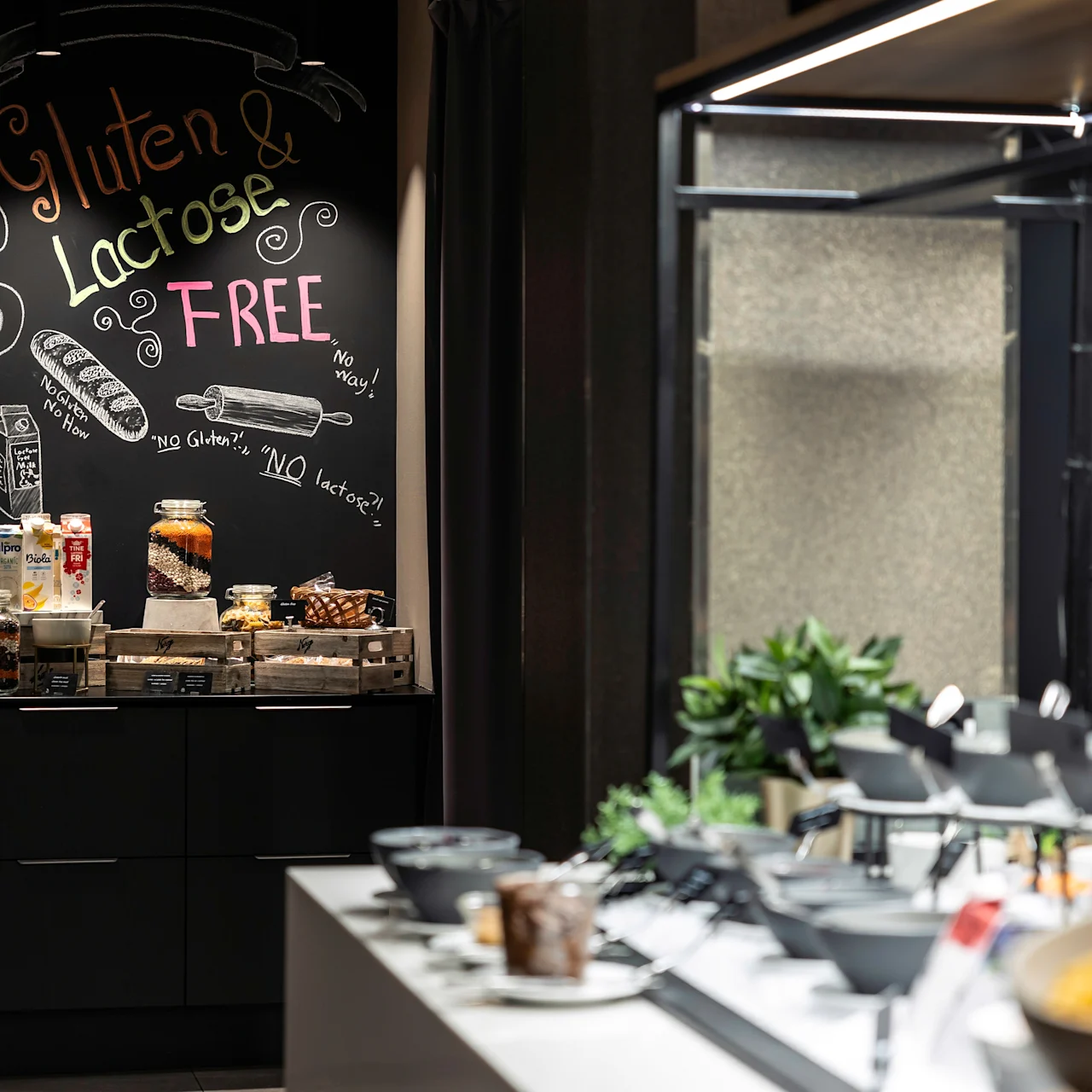 A chalkboard displays "Gluten & Lactose Free" in a buffet area. Various gluten-free and lactose-free food items are arranged below. Surrounding tables hold additional dishes. 