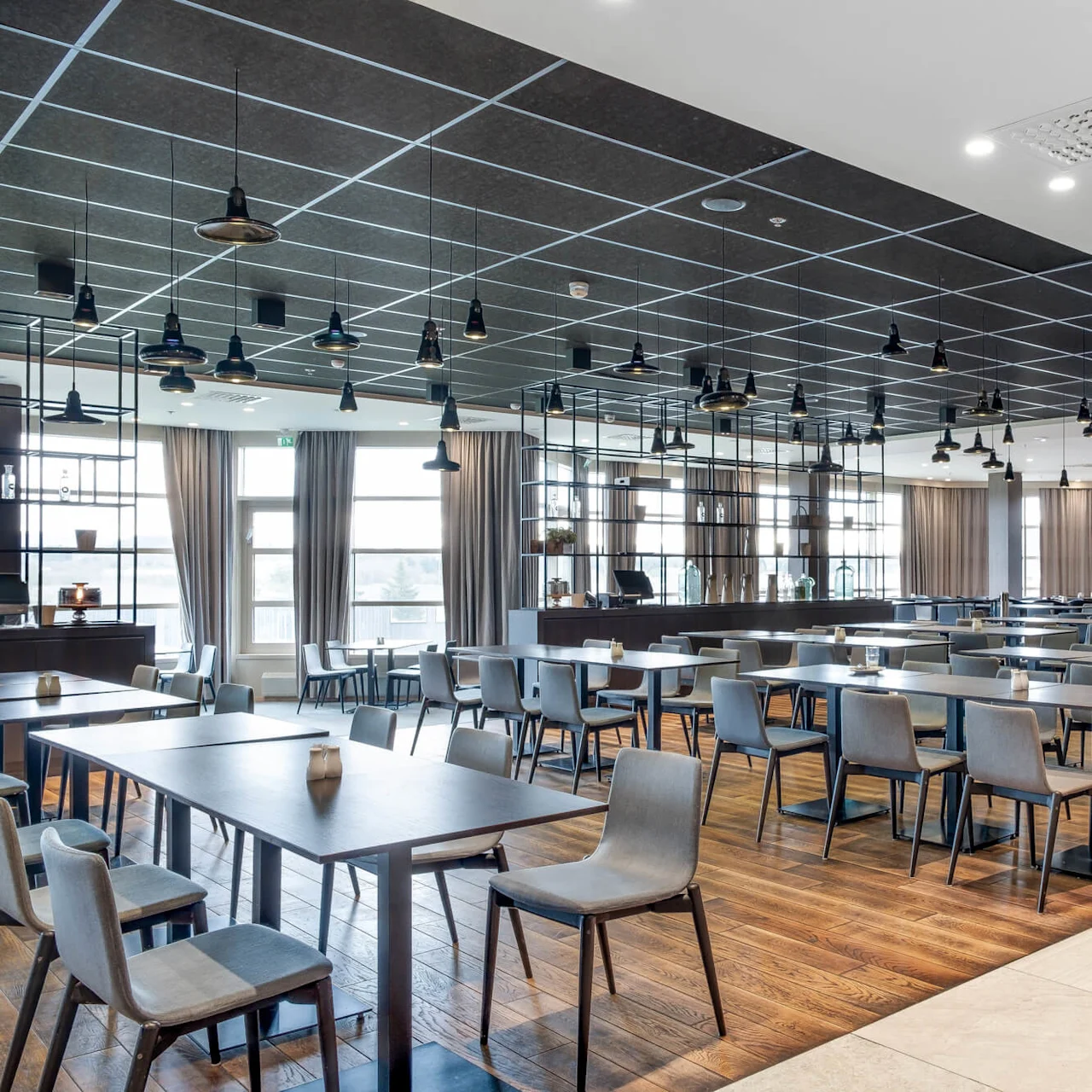 Modern restaurant interior with stylish furniture, hanging pendant lights, and a tall shelving unit displaying various items, in a spacious, airy setting.