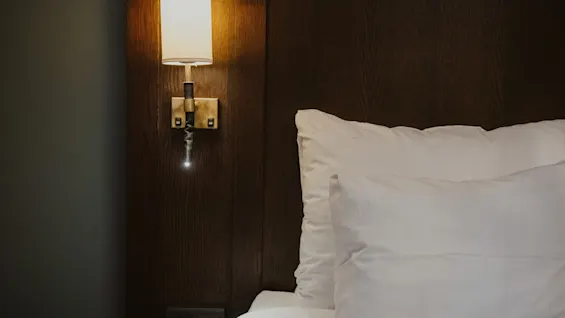 A cozy bedside scene at Home Hotel Kung Oscar with a warm lamp illuminating soft white pillows and bedding.