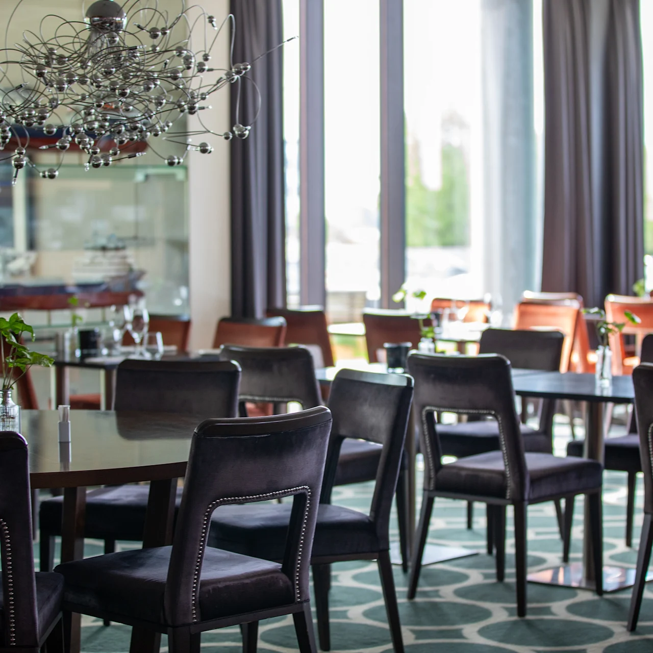 Spisebord er arrangert med svarte stoler i en moderne restaurant. Store vinduer slipper inn naturlig lys, og dekorative skipsmodeller er utstilt på hyller, noe som forsterker det nautiske temaet.