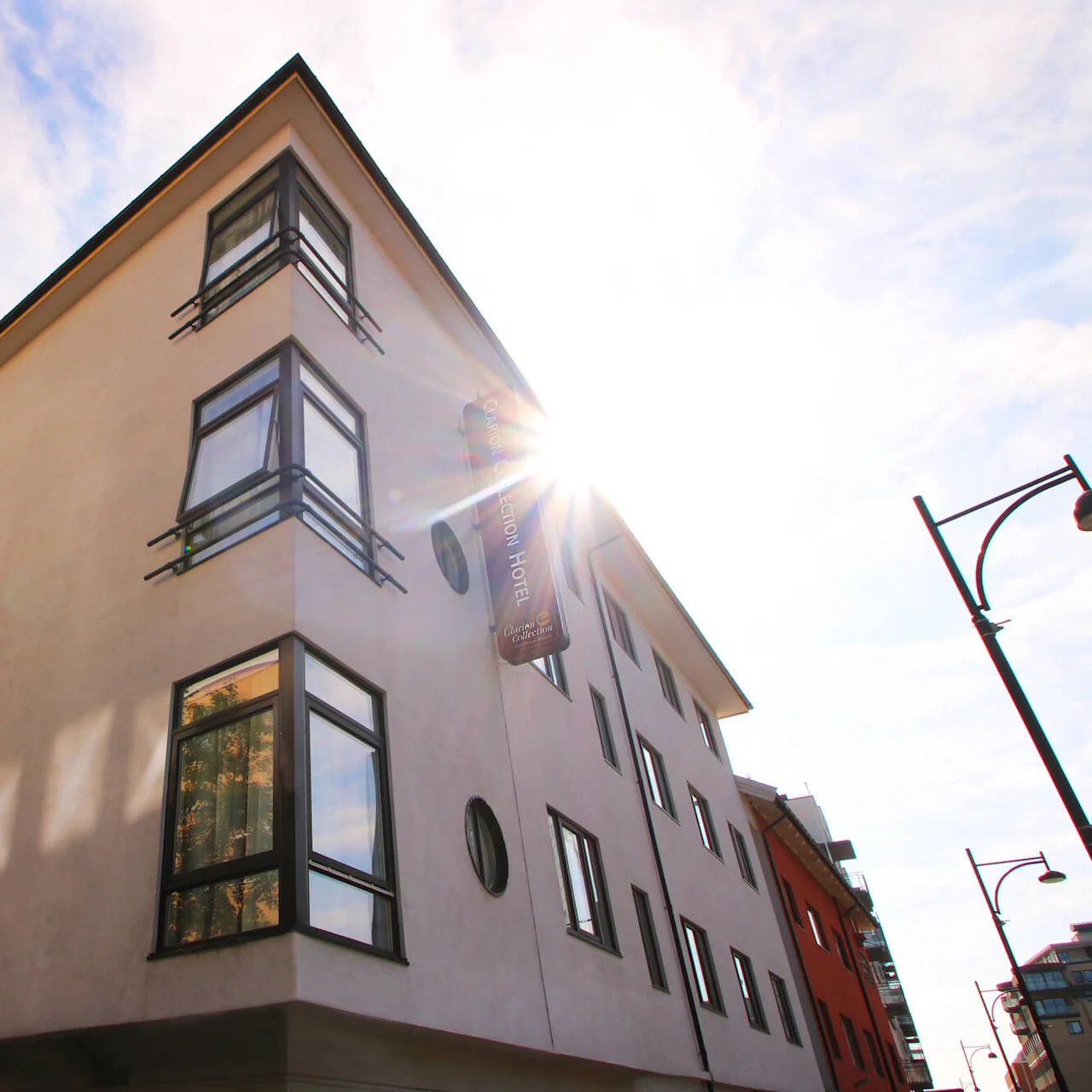 A modern building corner against a blue sky, sunlight flares from the edge.