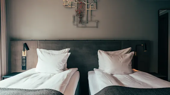 Two comfortable single beds with white bedding and dark grey blankets in a modern hotel room, ready for guests.