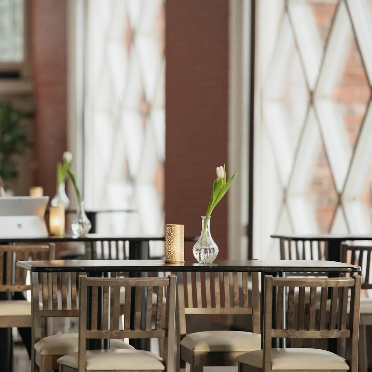 A woman works on a laptop while sitting at a table in a café with wooden chairs and vases holding tulips, surrounded by modern décor.